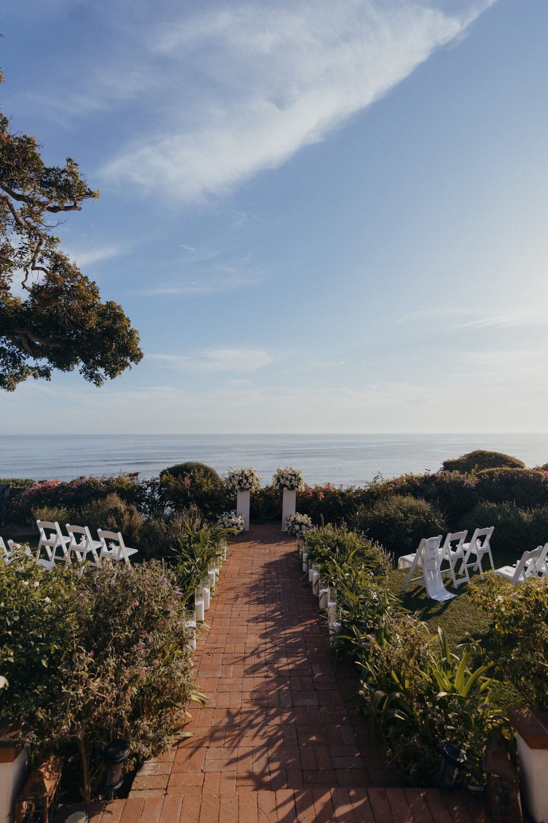 Ocean-view ceremony aisle lined with candles and white chairs