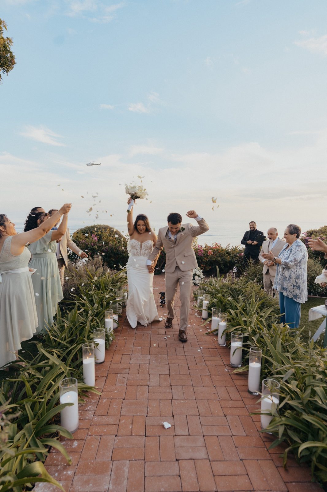 Couple walking back up a candlelit aisle as guests toss petals